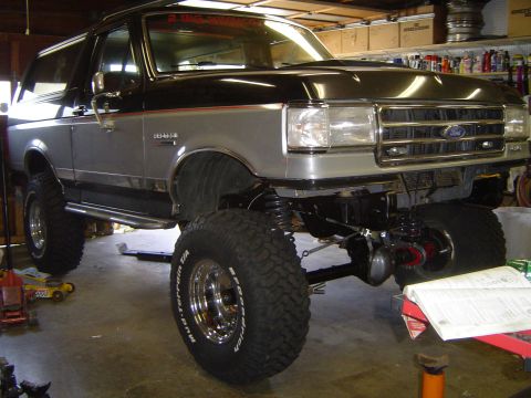 1989 Ford Bronco - A modified Ford Bronco is shown in a garage with its front axle and suspension components visible.