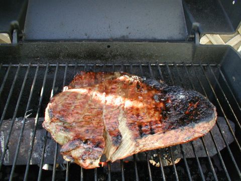 1979 Ford Bronco - A large cut of meat is being grilled outdoors.