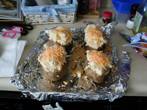 1979 Ford Bronco - Four baked potatoes topped with cheese sit on aluminum foil, ready for the oven.