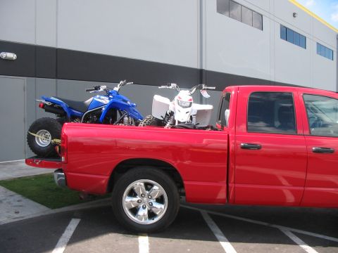 1980 Ford Bronco - A red pickup truck transports two all-terrain vehicles in its bed, viewed from the side.
