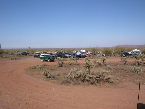 1984 Ford Bronco - A group of off-road vehicles and tents are set up in a desert area, with a prominent green 1984 Ford Bronco in the foreground.