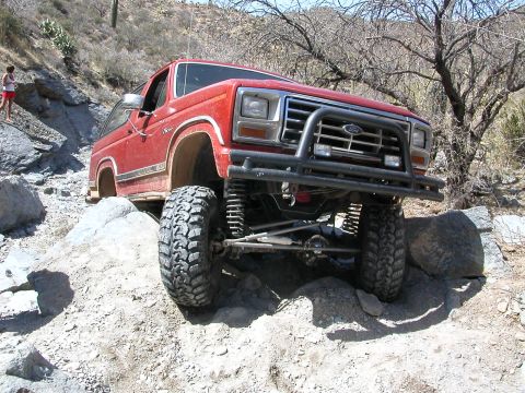 1984 Ford Bronco - Modified Ford Bronco tackling a challenging off-road trail with large rocks and steep inclines.