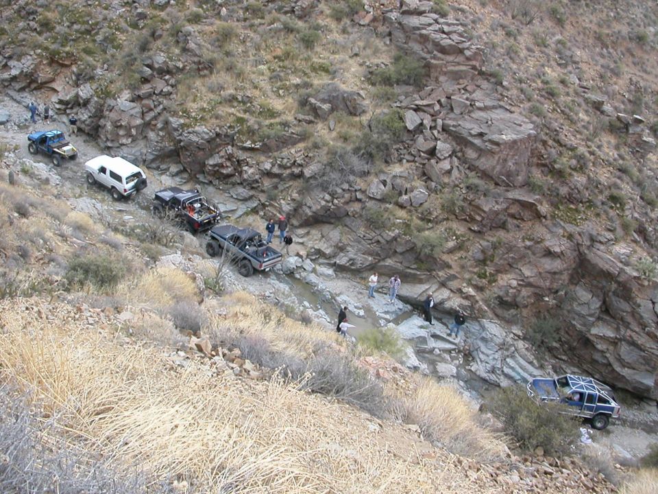 Several off-road vehicles navigate a steep, rocky mountain trail