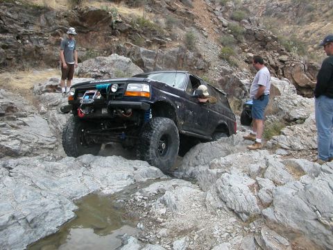 1984 Ford Bronco - A dark blue SUV tackles a challenging rocky terrain on an off-road trail.