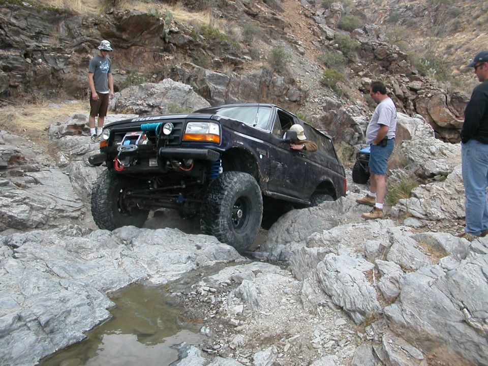 Dark blue SUV with off-road modifications navigating a rocky trail, with people watching