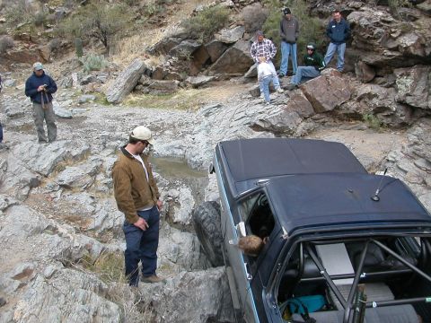 1984 Ford Bronco - Off-road vehicle stuck on rocks with spectators observing the difficult situation.