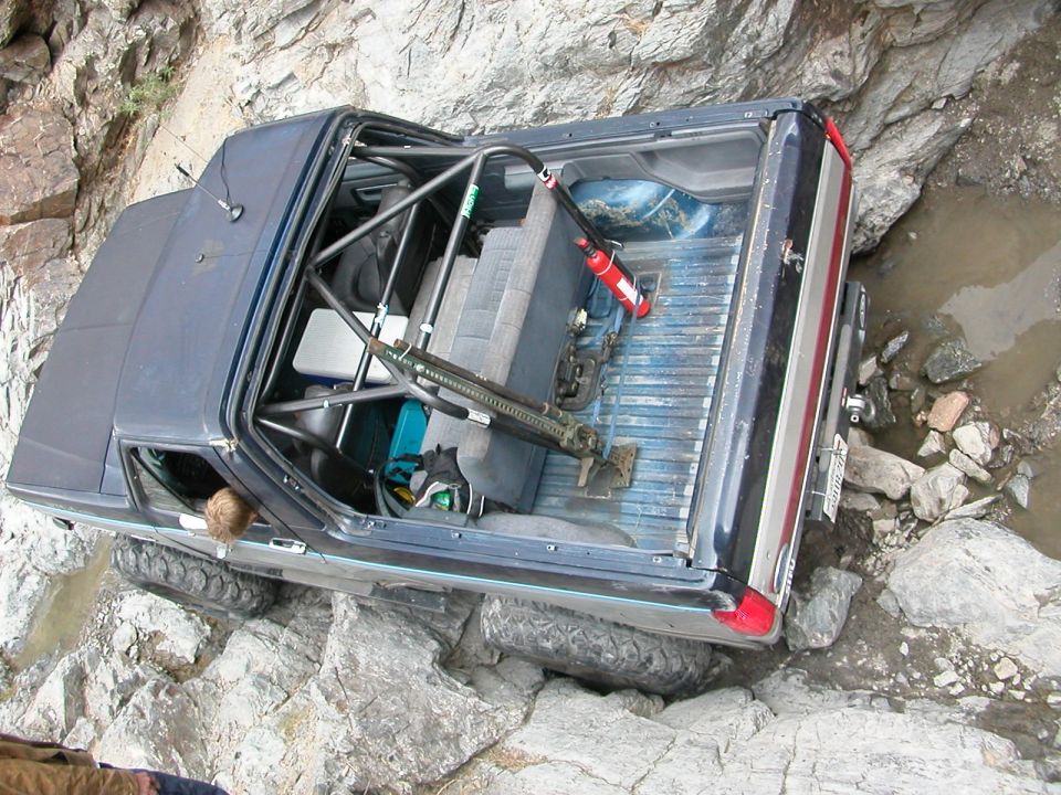 Off-road vehicle navigating a rocky trail, with a roll cage and jack visible inside