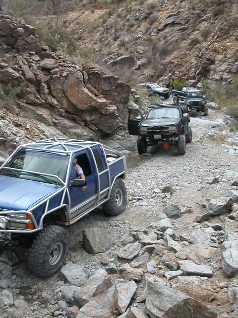 1984 Ford Bronco - Several off-road vehicles navigate a rough, rocky trail in a canyon.