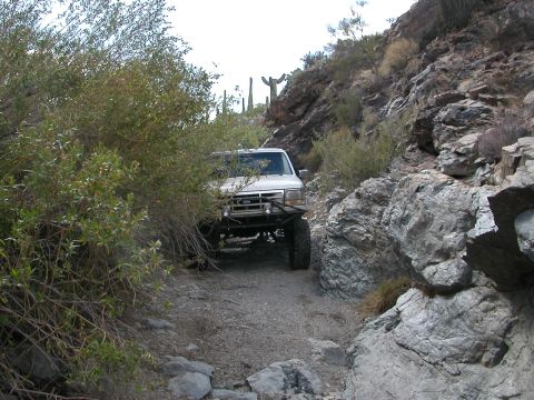 1984 Ford Bronco - White Ford Bronco on a rough, rocky trail in a desert environment.