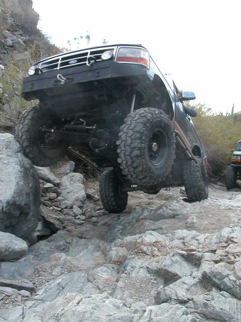 1984 Ford Bronco - This modified Ford Bronco is navigating a rocky off-road trail, with another vehicle in the distance.
