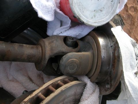 1984 Ford Bronco - Close-up view of a driveshaft U-joint and a brake rotor, partially covered by towels and a can.
