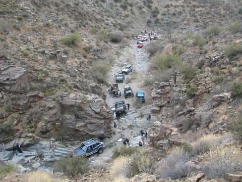 1984 Ford Bronco - A convoy of off-road vehicles navigates a challenging trail through a desert landscape.