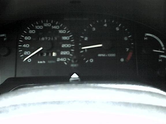 Instrument cluster speedometer in km/h reading ~187213 km with tachometer, dim backlighting