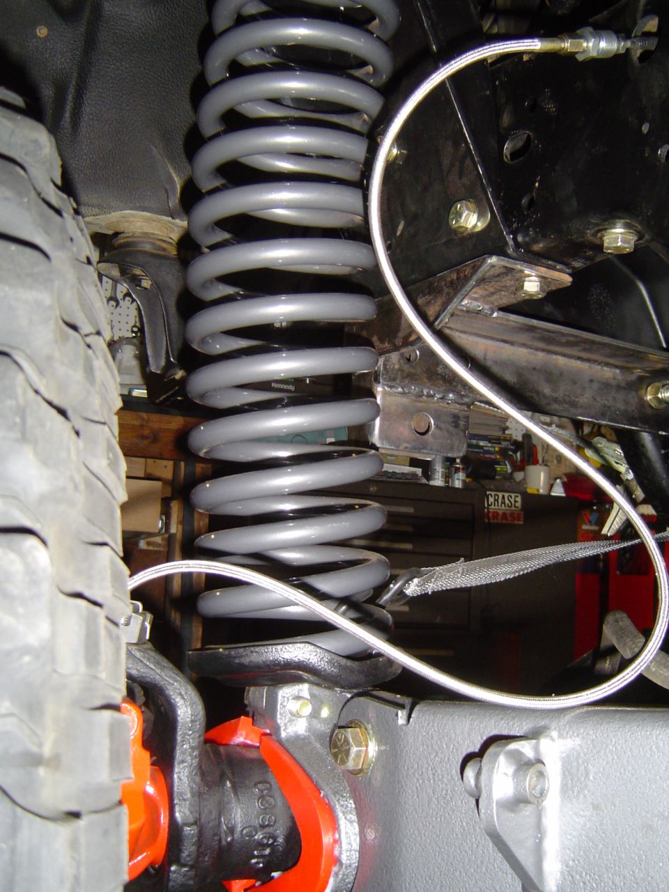 Gray coil spring, radius arm bracket and braided brake line on a lifted 4x4 front axle