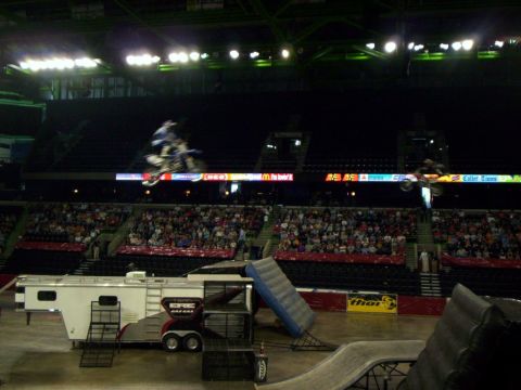 1986 Ford Bronco - Freestyle motocross rider in blue gear soaring over an arena floor on a blue and white bike while a second rider launches at right, both ab…