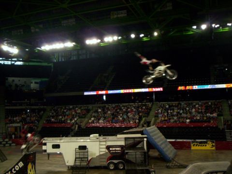 1986 Ford Bronco - Freestyle motocross rider stretched over the handlebars of a white and red dirt bike high above an indoor arena, with a second rider blurre…