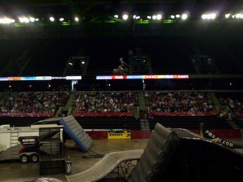 1986 Ford Bronco - Freestyle motocross rider caught mid-jump high over an arena, silhouetted above a lit scrolling sponsor ring showing Coca-Cola, H-E-B and M…
