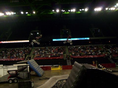 1986 Ford Bronco - Motocross riders perform aerial stunts in an indoor arena filled with spectators.