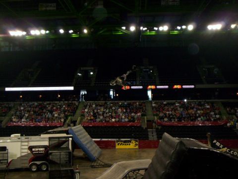 1986 Ford Bronco - Freestyle motocross rider silhouetted upside down in a backflip high over an arena, above the LED ribbon board and grandstands. The floor f…