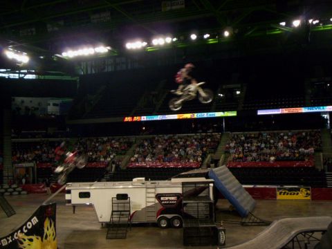 1986 Ford Bronco - Two freestyle motocross riders in the air at once inside an arena, one soaring high across the LED ribbon board and another blurred in a tr…