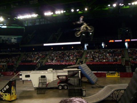 1986 Ford Bronco - Freestyle motocross rider hangs off the rear of a white dirt bike in mid-air high above an arena floor, legs kicked out behind. A white Tea…