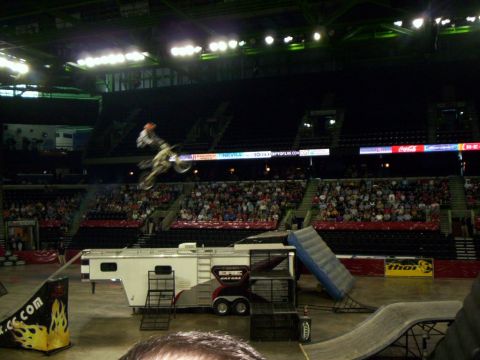 1986 Ford Bronco - A motocross rider performs a jump over a trailer during an indoor event.