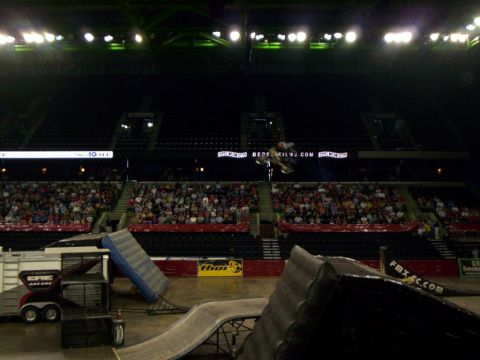 1986 Ford Bronco - Motocross rider blurred mid-flip over the arena floor, level with a dark upper deck and a lit Depth Films sponsor board. In the foreground…