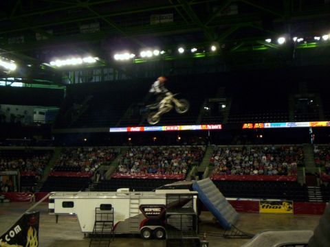 1986 Ford Bronco - Freestyle motocross rider hangs off the back of a white dirt bike in mid-air over an arena floor, framed by an illuminated ring of Coca-Col…