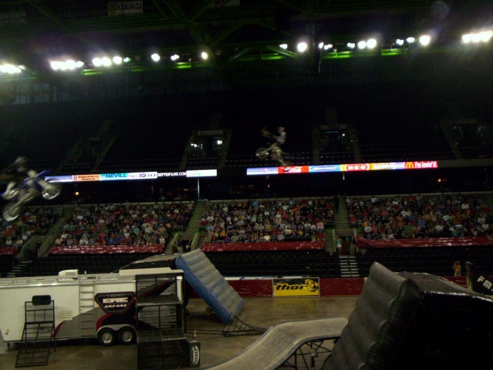 motocross riders mid-air jump inside arena with crowd watching