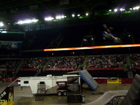 1986 Ford Bronco - A motocross rider performs a jump inside a stadium, with a trailer and ramp set up on the arena floor.