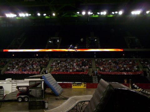 1986 Ford Bronco - A blue dirt bike hangs nose-down mid-rotation in front of the flame-lit ribbon board of an indoor arena, its rider stretched above the mach…