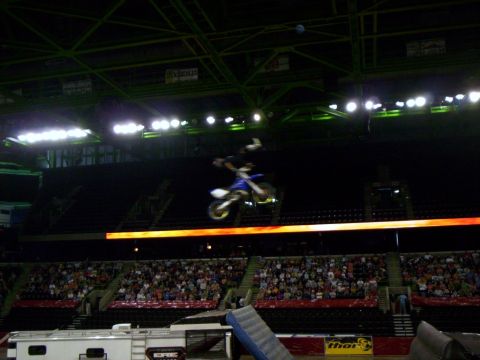 1986 Ford Bronco - Freestyle motocross rider in a superman-style extension above a blue and white dirt bike, high enough to be framed against the arena's gree…
