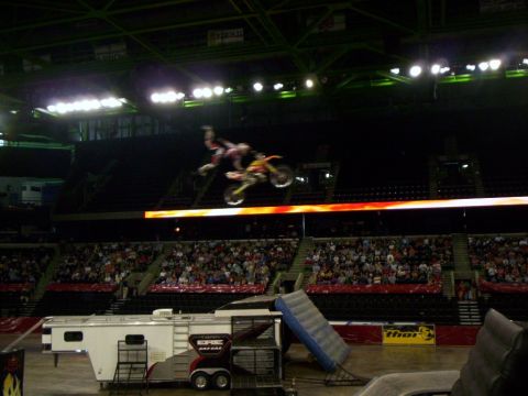 1986 Ford Bronco - Freestyle motocross rider in red gear hanging off the side of a red and yellow dirt bike mid-jump above an arena's flame-graphic ribbon boa…