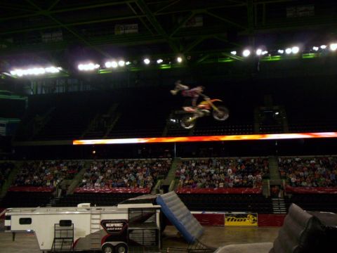 1986 Ford Bronco - A motocross rider performs a jump in an arena, with a trailer and ramps visible below.