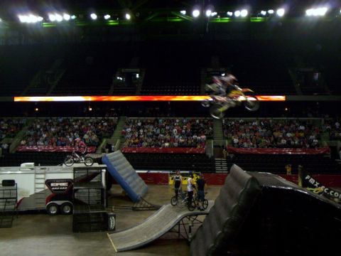 1986 Ford Bronco - Performers execute aerial maneuvers on dirt bikes in an indoor stadium before a seated audience.