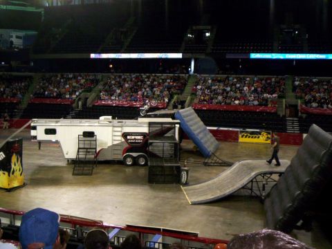 1986 Ford Bronco - A motocross rider performs a jump inside an arena with a large trailer and ramps set up.