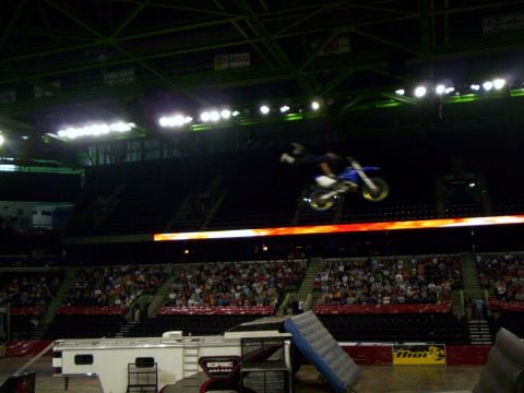 1986 Ford Bronco - Freestyle motocross rider extended fully off the back of a blue and white dirt bike with yellow rims, flying above the flame-graphic ribbon…