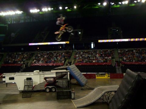 1986 Ford Bronco - Freestyle motocross rider high above an arena floor, upside down over an orange and white dirt bike in the middle of a flip. A white Team G…