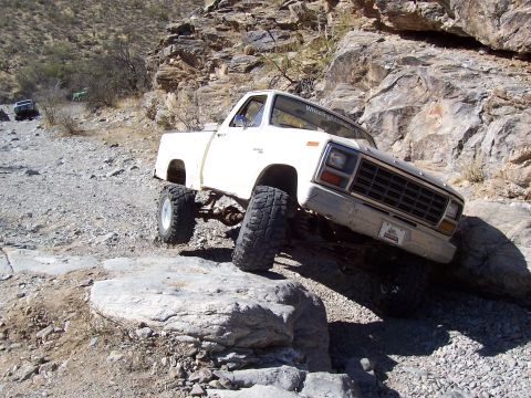 1981 Ford F-150 - White pickup truck is off-roading on a rocky trail, with another vehicle in the distance.