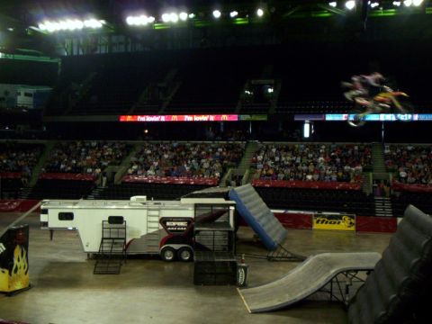 1986 Ford Bronco - A motocross rider performs a jump in an arena, with ramps and a trailer set up for the event.