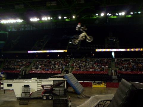 1986 Ford Bronco - Freestyle motocross rider throws a trick high over an arena floor, body extended above a white dirt bike with the front wheel tipped up. Be…