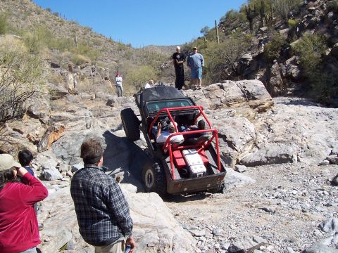 1981 Ford F-150 - A modified off-road vehicle navigates a challenging rocky trail with spectators watching.