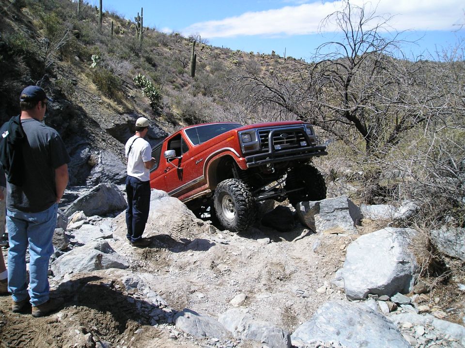 Red 1993 Ford Bronco on rocky trail, front-right wheel lifted