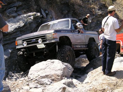 1993 Ford Bronco - This heavily modified Ford Bronco is tackling a challenging off-road course with spectators present.