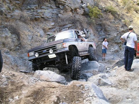 1993 Ford Bronco - This lifted Ford Bronco navigates a rocky off-road path with a driver and passengers.