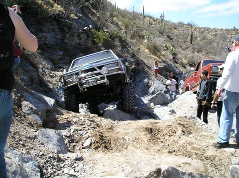 1993 Ford Bronco - Two off-road vehicles tackle a challenging rocky terrain with onlookers present.