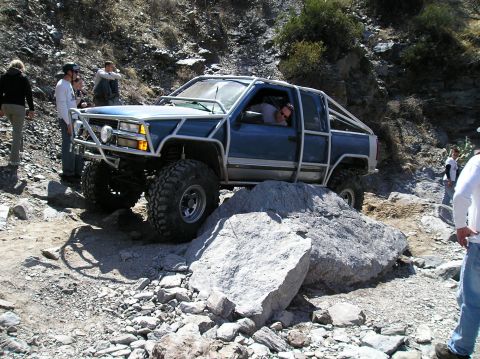 1993 Ford Bronco - Modified pickup truck tackling a rocky off-road course with spectators watching.