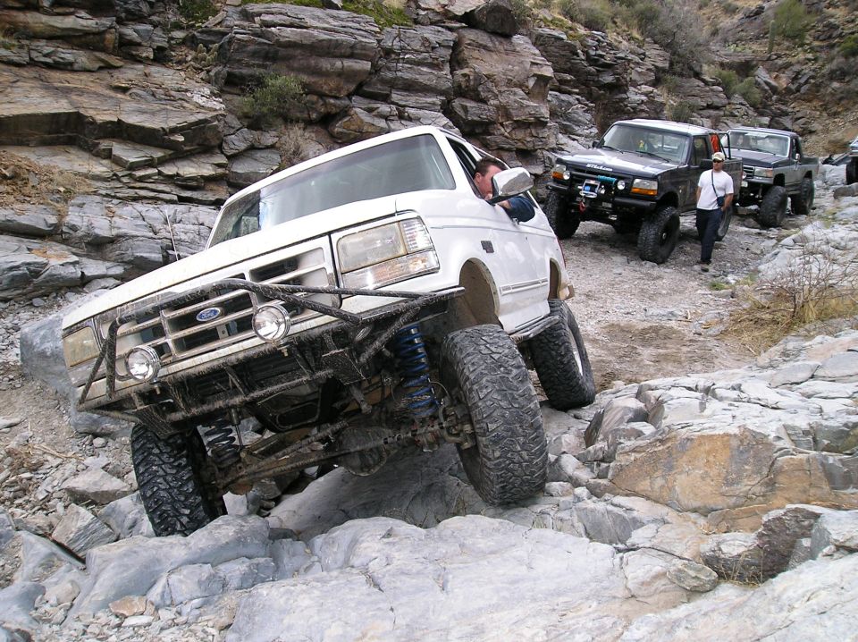 White Ford Bronco with aftermarket bumper and large tires navigating a rocky trail