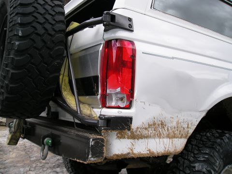 1993 Ford Bronco - Rear view of a white 1993 Ford Bronco, showing a spare tire mounted on the back and a damaged taillight.