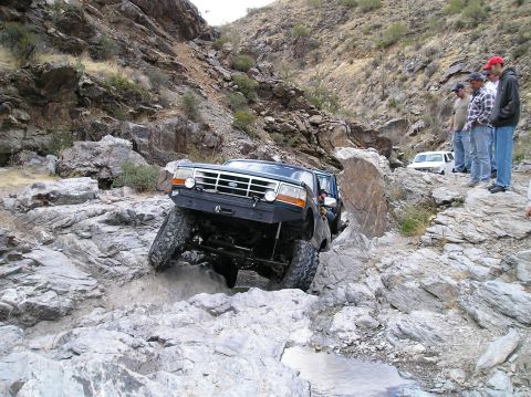 1993 Ford Bronco - A lifted 1993 Ford Bronco tackles a challenging rocky off-road course, with onlookers observing.